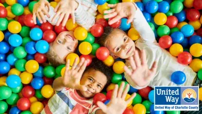 three children in a ball pit holding their hands up